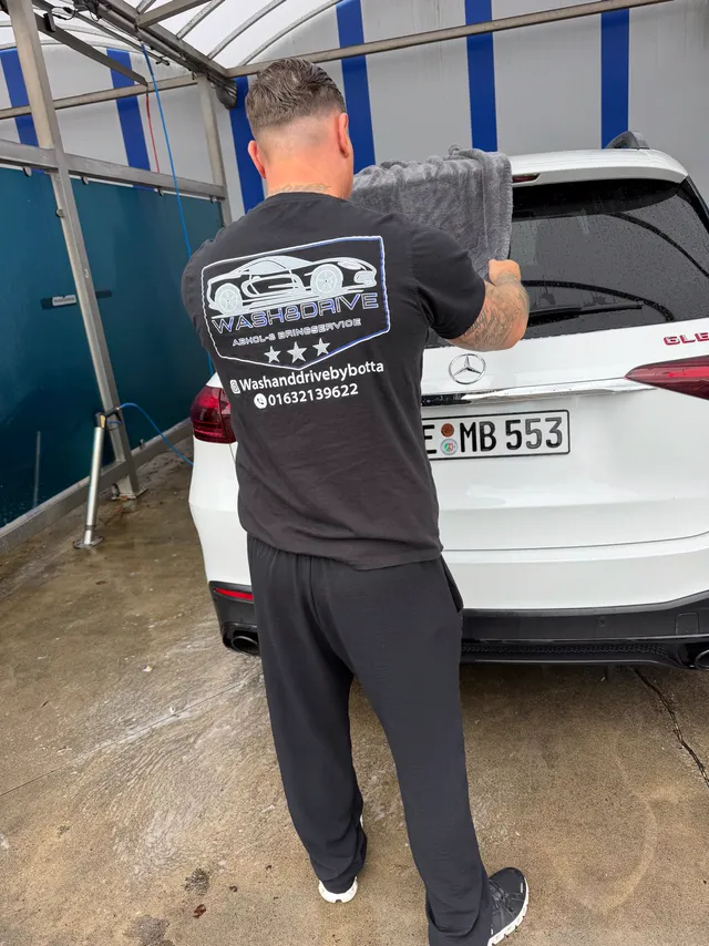 Weißer Mercedes GLE wird in der Waschbox abgetrocknet – auf dem Shirt das Wash & Drive Logo
