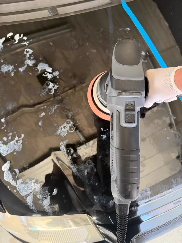 Poliermaschine mit Pad auf einer schwarzen Motorhaube, Kanten mit blauem Klebeband abgeklebt